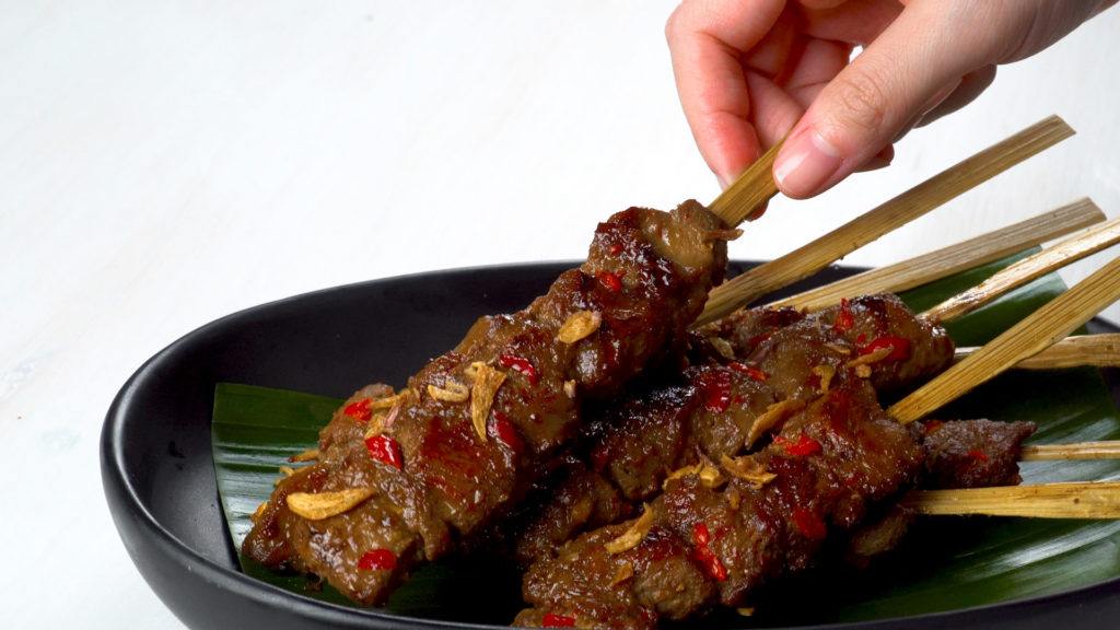 Sate rembiga khas Lombok tersaji di atas piring hitam.