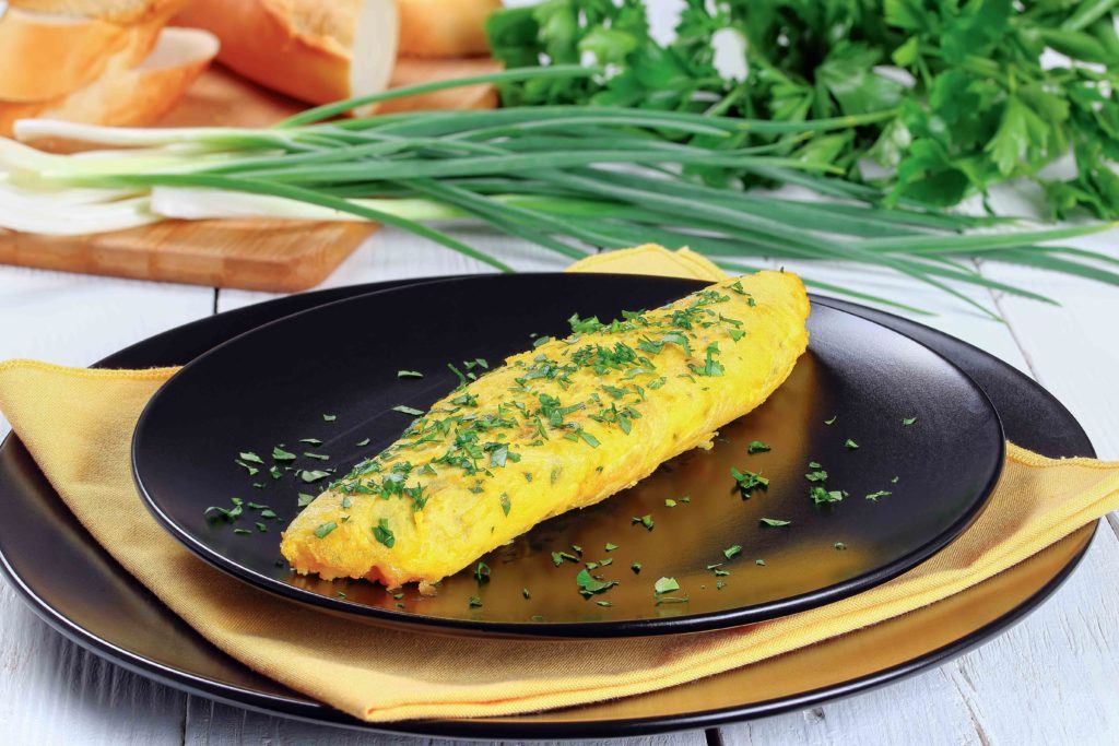 Omelet Prancis tersaji di atas piring hitam.