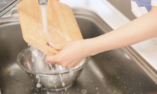 Tangan perempuan membersihkan talenan kayu di westafel
