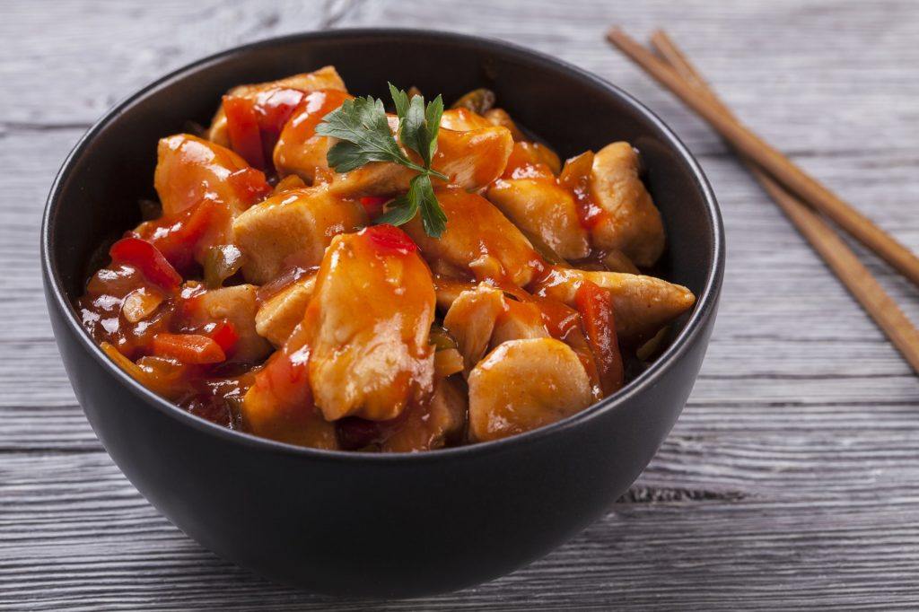 Hasil masak resep ayam pedas saus merah dalam mangkuk dan berlatar kayu serta sumpit.