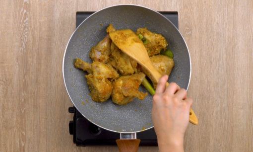 Ayam ditumis dengan bumbu gulai kuning dalam wajan dengan spatula kayu