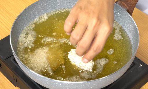 Ayam berbalut tepung dimasukkan ke dalam minyak goreng di dalam wajan.