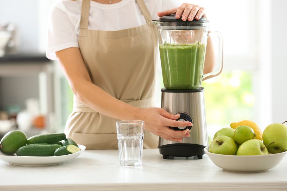 Seorang wanita tengah menggunakan blender untuk sayur dan apel.