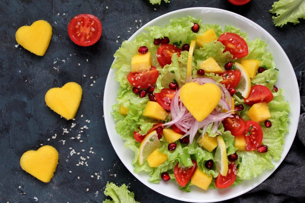 Satu piring salad buah dan sayur di atas alas gelap.