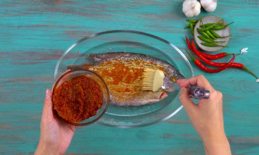 Ikan gurame dioleh bumbu merah menggunakan kuas.