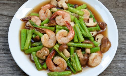 Tumis udang vaname dengan jamur dan asparagus terhidang di atas piring.