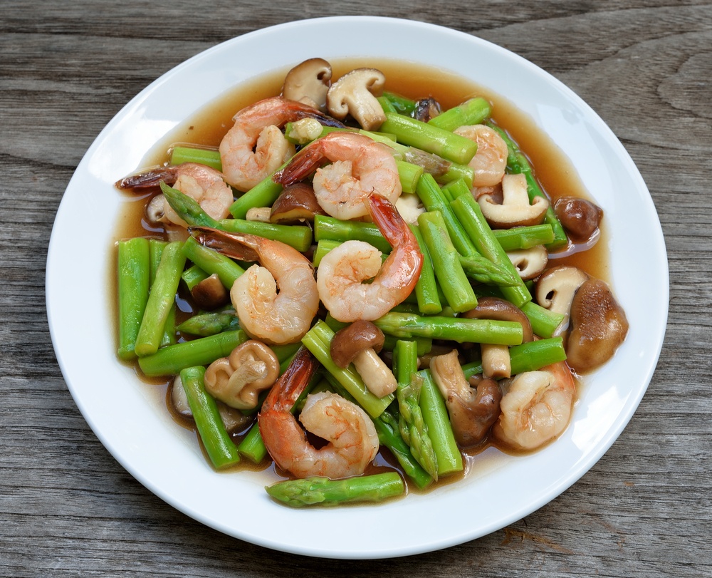 Tumis udang vaname dengan jamur dan asparagus terhidang di atas piring.