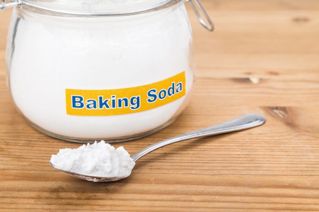 Satu toples kaca baking soda dengan satu sendok di hadapannya.