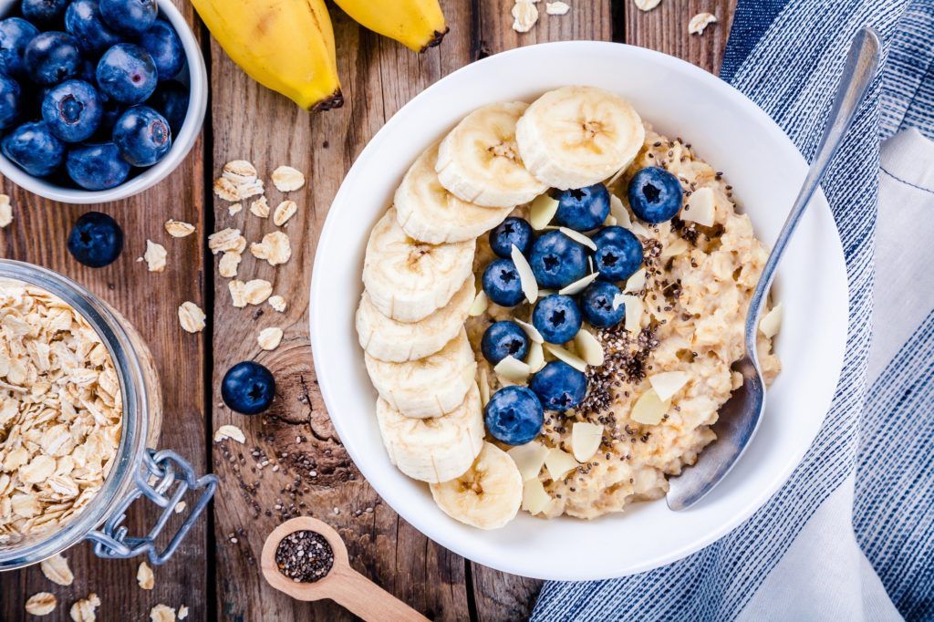 Satu mangkuk oatmeal bertabur blueberry dan potongan pisang.