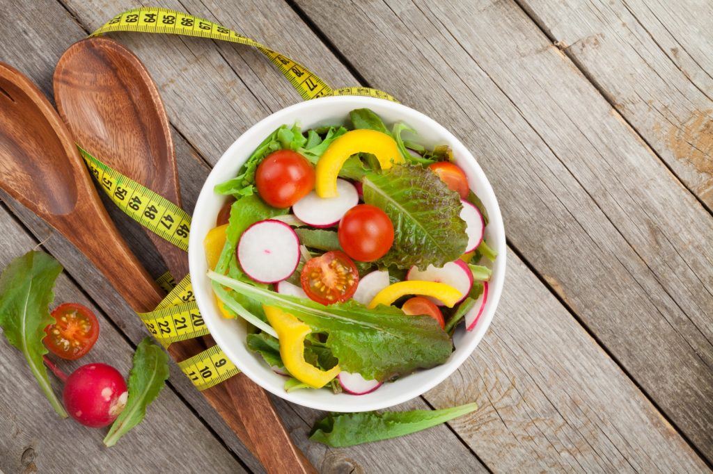 Diet kenyang dengan satu mangkuk sayuran dengan sendok kayu dan meteran pita di belakangnya.