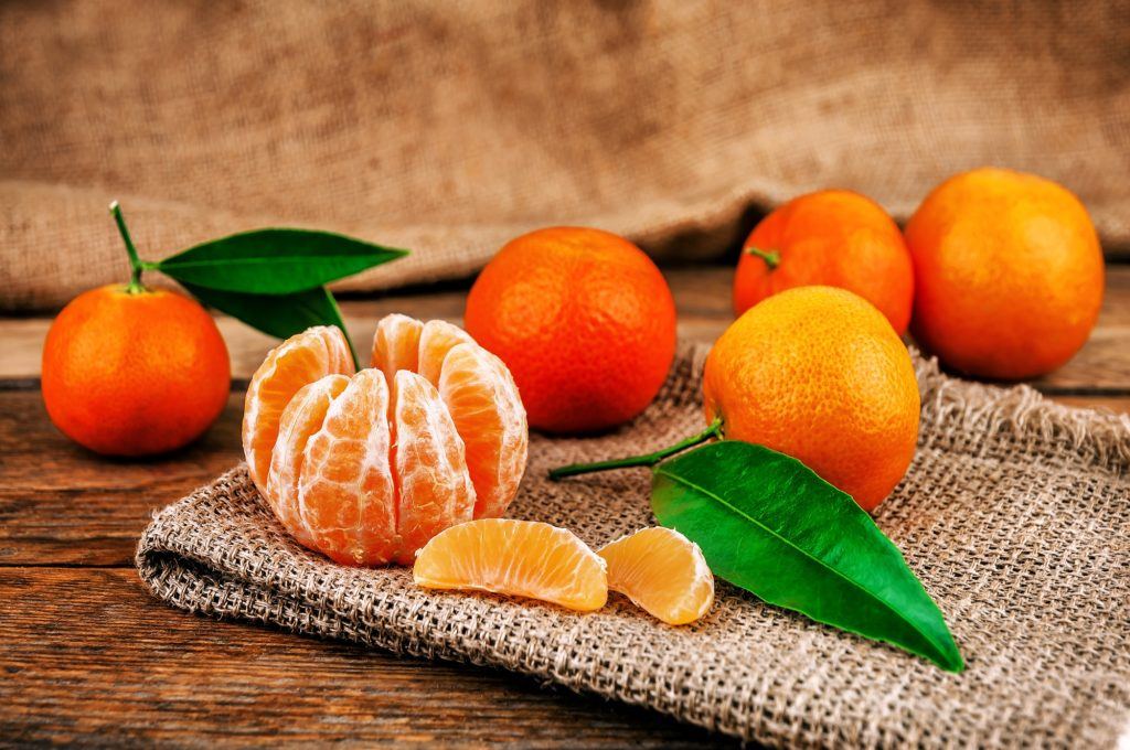 Jenis jeruk mandarin terkupas dan jeruk yang belum dikupas di belakangnya.