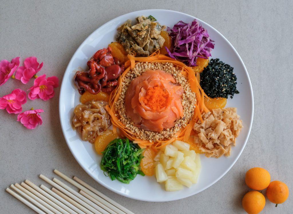 Satu piring yusheng dengan sumpit dan bunga di sampingnya.