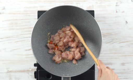 Potongan daging ayam ditumis bersama bumbu di atas wajan dengan spatula cokelat.