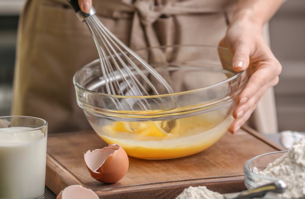 Seorang chef tengah menggunakan whisk untuk mengocok telur dalam mangkuk.