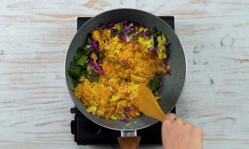 nasi goreng gila dengan berbagai topping sayuran sedang diaduk memakai spatula di atas wajan