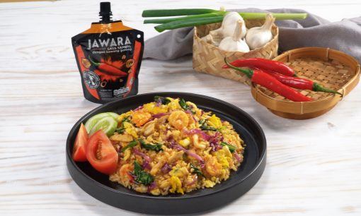 nasi goreng gila dalam piring hitam dengan sambal jawara dan rempah di belakangnya