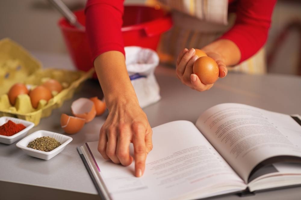 Seorang wanita tengah memegang telur dan mempelajari resep.