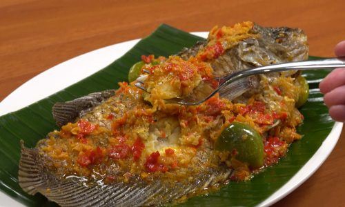 Pecak ikan gurame tersaji di atas piring beralaskan daun pisang, masakan ikan.