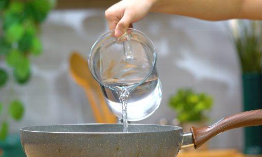 Menuangkan air ke dalam wajan untuk memasak semur ayam.