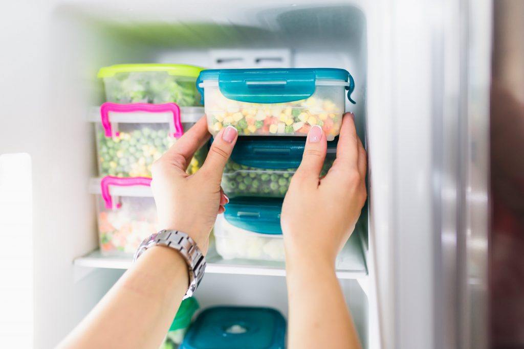 Tangan menyimpan container bahan makanan dalam kulkas.