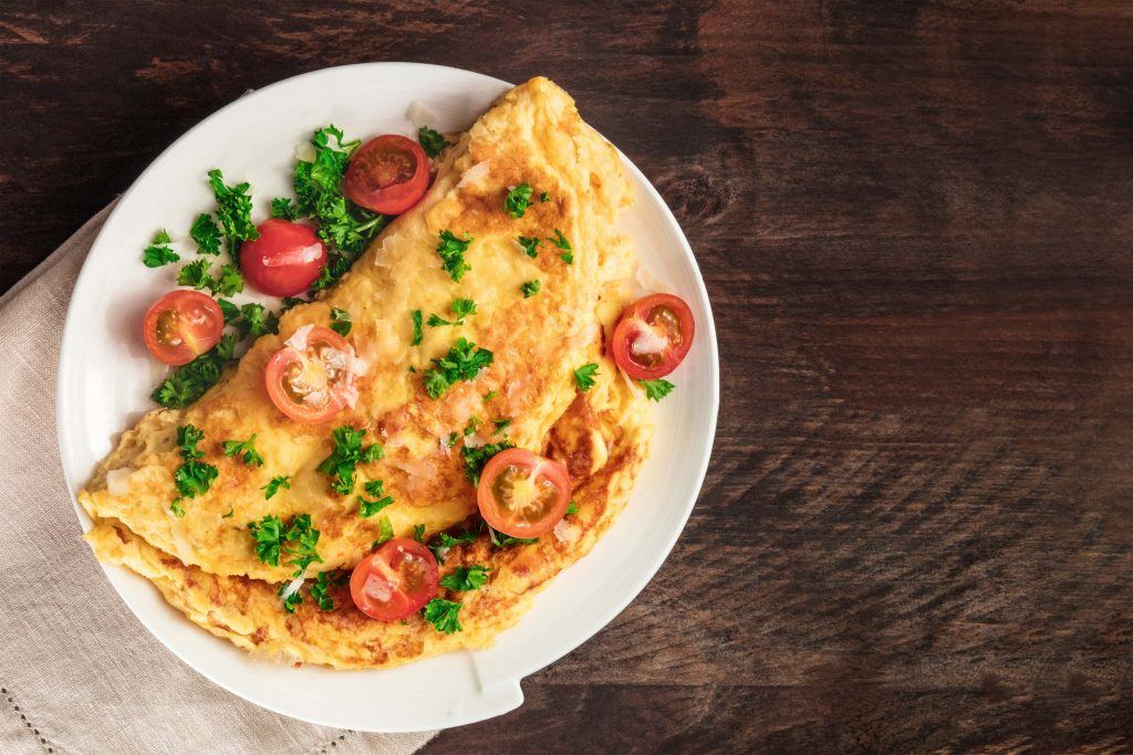 Resep mudah berupa dadar telur lengkap dengan tomat cherry tersaji di atas piring putih yang beralaskan napkin dan meja kayu cokelat tua.