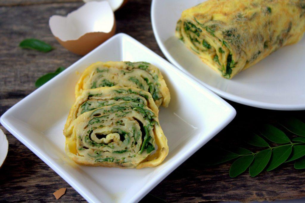 Telur gulung daun kelor dipotong dan disajikan di atas piring putih.