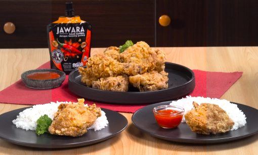 Dua piring ayam goreng krispi dengan nasi hangat dan saus sambal disajikan beserta ayam goreng lainnya dalam piring besar.