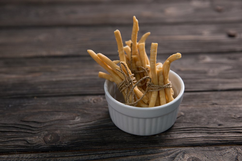 Mangkuk kecil berisikan hasil resep kue bawang keju yang diikat dan diletakkan di atas meja kayu.