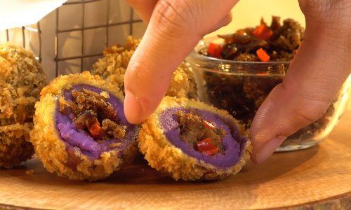 Hasil memasak resep bola ubi ungu tersaji di atas meja kayu dan tengah dinikmati.
