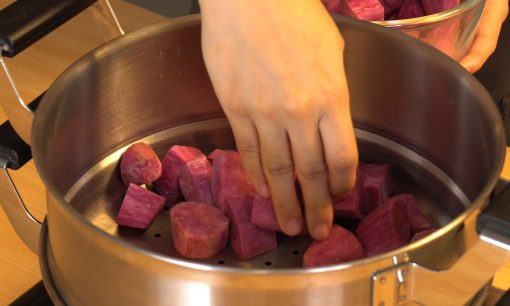 Tangan chef menyimpan potongan ubi ungu di dalam kukusan.