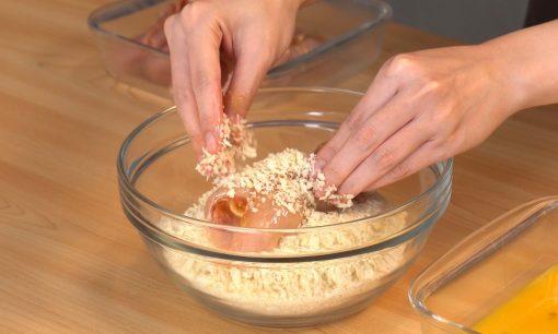 Daging ayam fillet digulingkan ke dalam tepung panir dalam mangkok kaca.