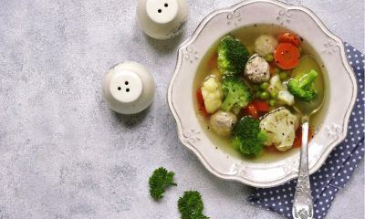 Satu piring sup berisi kembang kol, brokoli, wortel, di atas napkin polkadot dengan sendok.