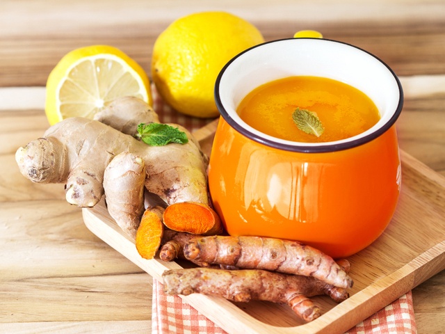 Segelas minuman herbal untuk meningkatkan daya tahan tubuh tersaji di atas nampan kayu dan didampingi jahe serta buah lemon di atas napkin kotak-kotak.