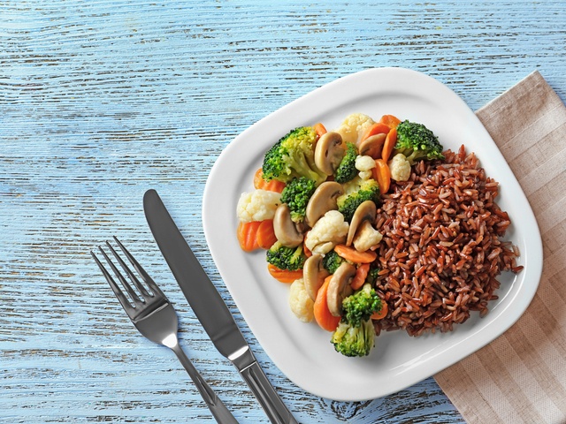 Sepiring menu sahur sehat berupa nasi merah dan sayuran dengan garpu dan pisau di sampingnya