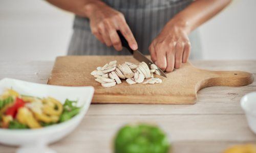 Tangan wanita memotong jamur di atas tatakan kayu merancang menu buka puasa dan sahur sebulan.