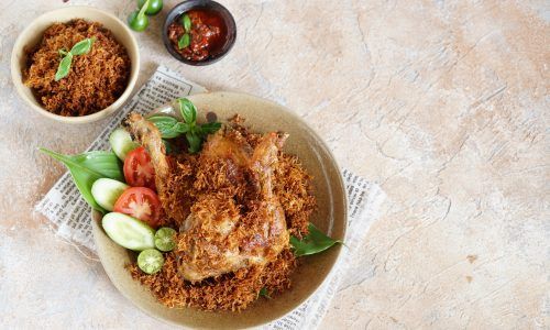 Sepiring kreasi masakan ayam goreng serundeng kelapa bersama sambal di sampingnya.