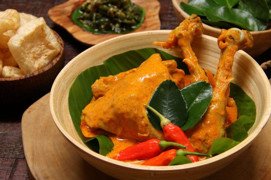 Sepiring masakan gulai ayam Padang dengan sambal hijau di belakangnya.