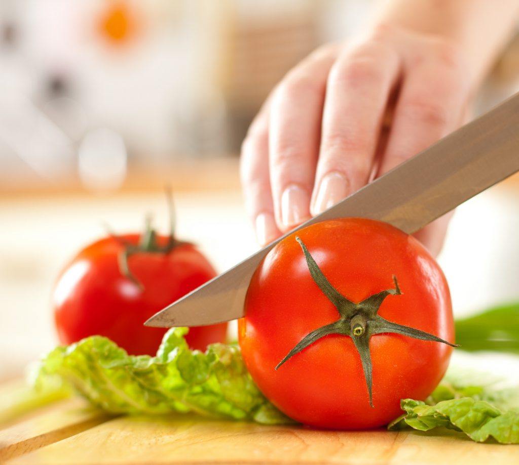 Tangan mengiris tomat dengan pisau