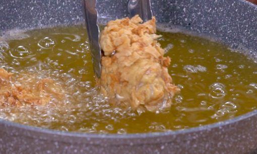 Proses penggorengan ayam dalam wajan berisi minyak untuk resep nasi ayam rice cooker.