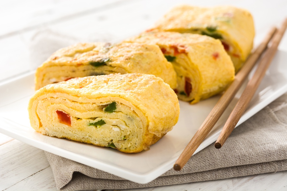 Tamagoyaki tersaji di atas piring putih bersama sumpit.