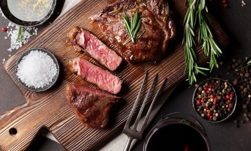 Daging steak dipotong sebagian di atas papan kayu.