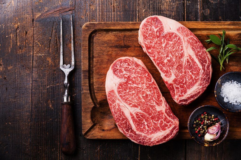 Dua potong steak dengan marbling yang cantik di atas papan kayu