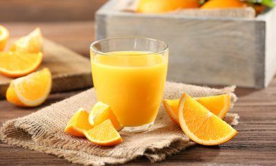 Segelas jeruk hangat segar didampingi potongan buah dan disajikan di atas napkin serta meja kayu.
