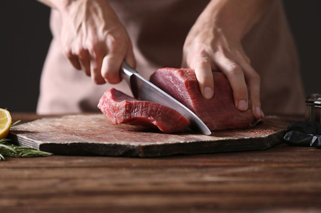 Tangan chef memotong daging di atas talenan dengan pisau