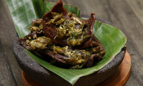 Seporsi lidah sapi cabai hijau tersaji di atas piring beralaskan daun pisang.