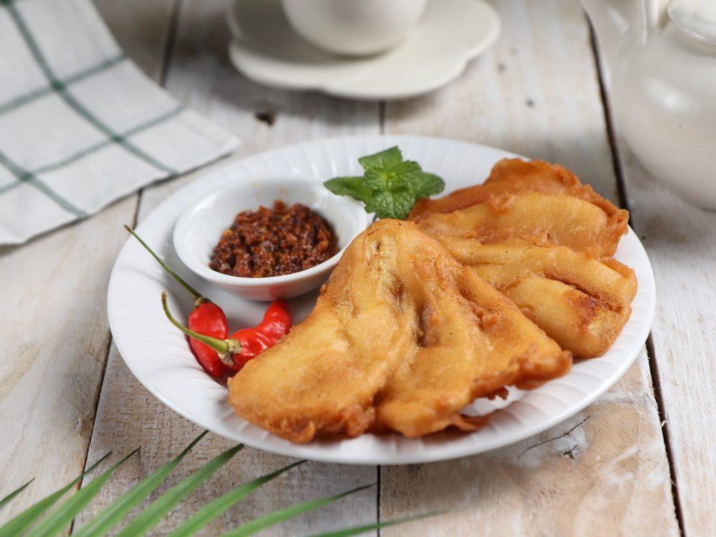 Pisang goreng sambal roa disajikan di atas piring yang diletakkan di atas meja kayu aneka gorengan.