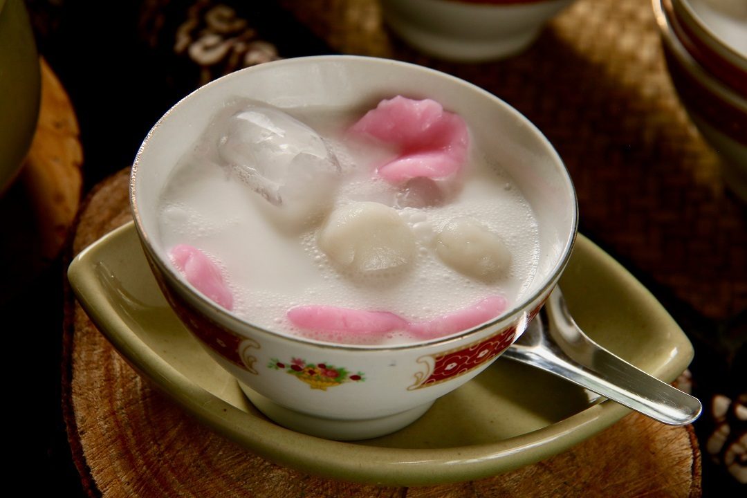 Semangkuk es gempol yang merupakan olahan dari tepung beras di atas nampan cokelat dengan sendok di bawahnya