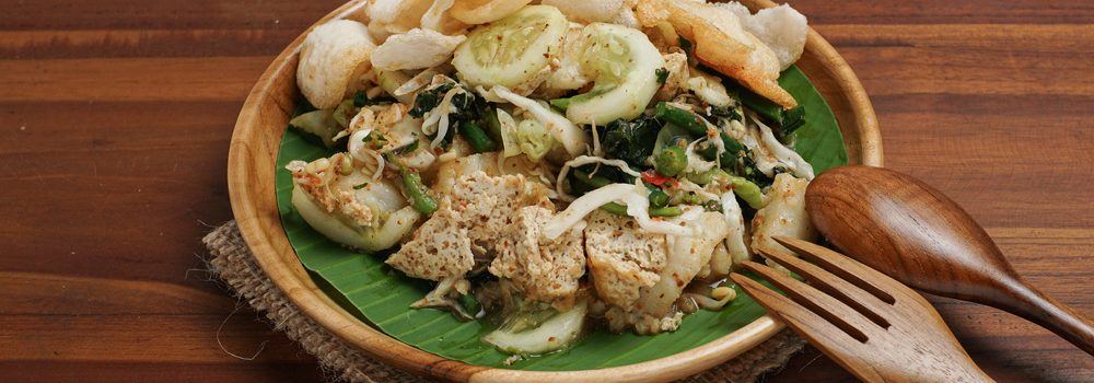 Hasil masak menu sayur resep lotek Bandung beralas daun pisang hijau di piring cokelat dan sendok garpu.