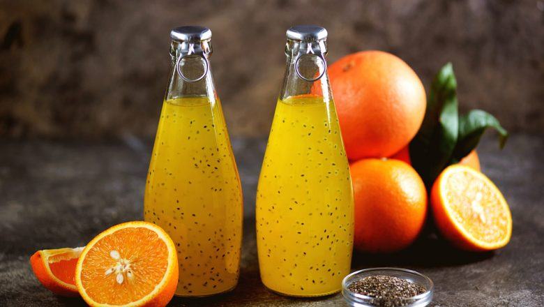 Dua botol berisikan jus jeruk dengan buah-buahan dan chia seed di sekelilingnya.