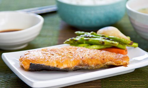 Satu piring berisikan olahan ikan salmon panggang yang disajikan dengan nasi dan sup.